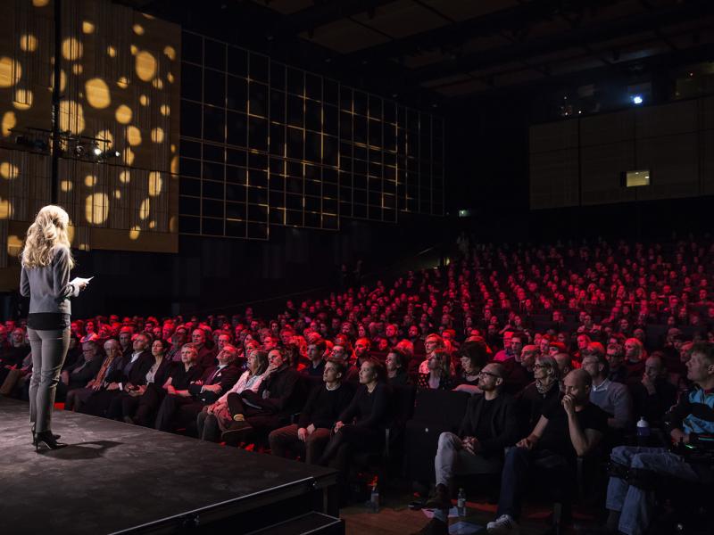 En kvinde står på scenen i Det Kongelige Biblioteks Dronningesal foran publikum.